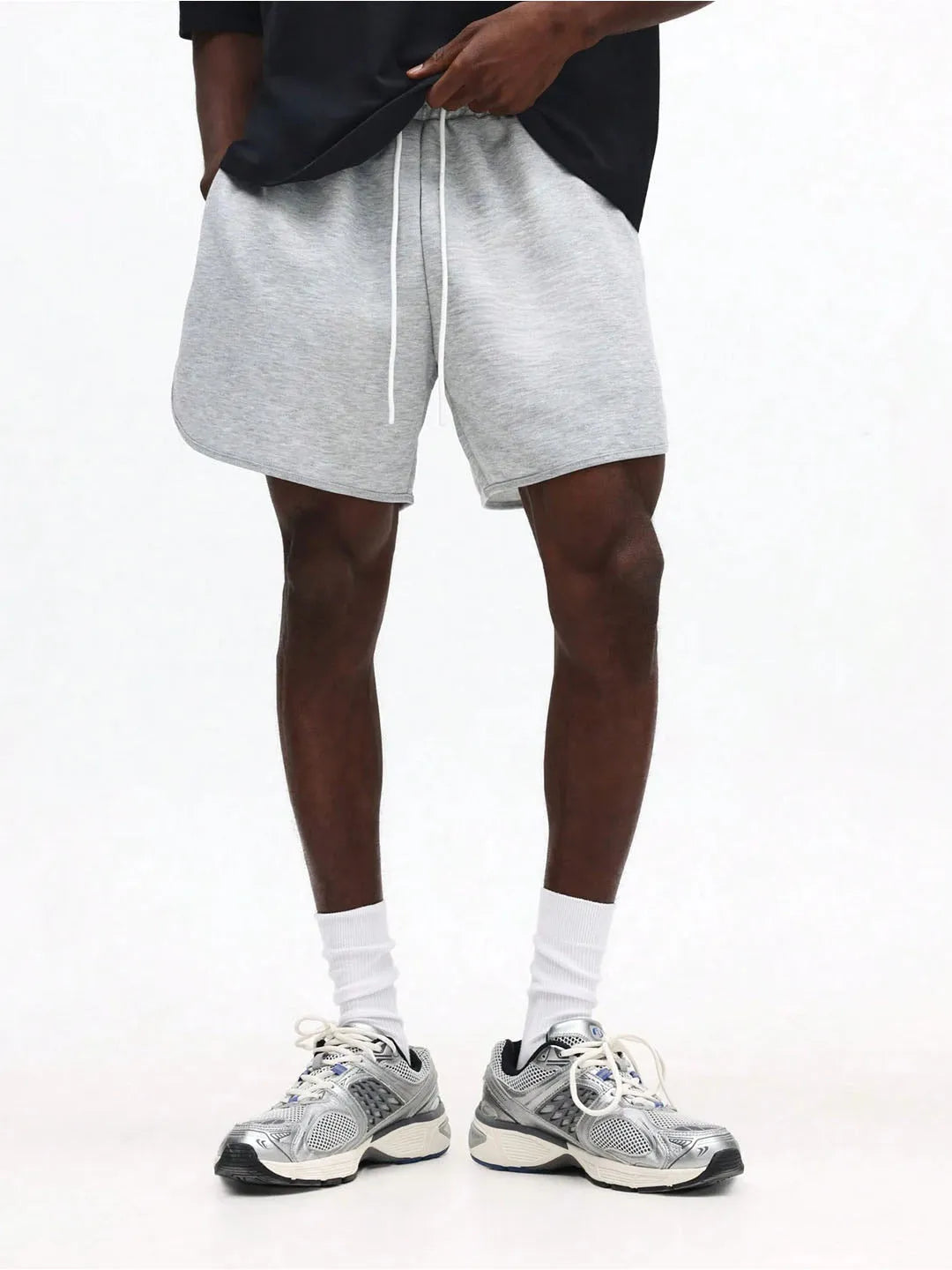 Person wearing grey shorts and white sneakers on a white background