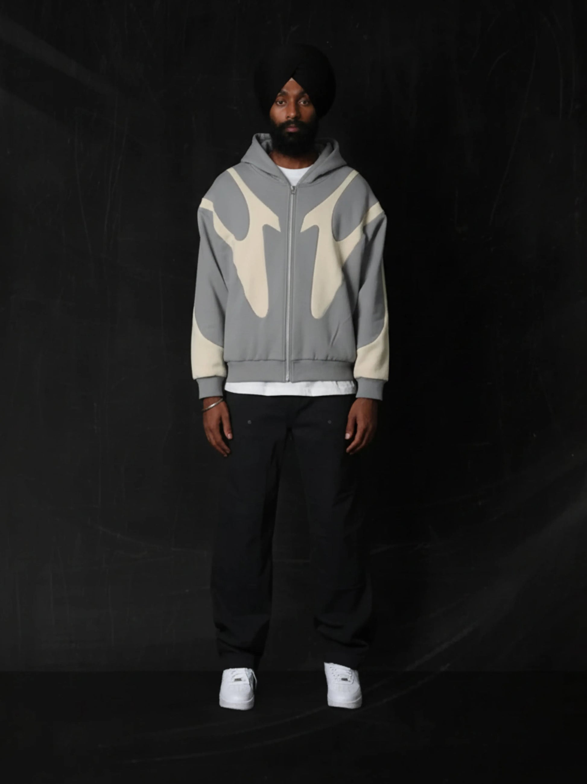 Person wearing a grey hoodie with abstract designs on a black background