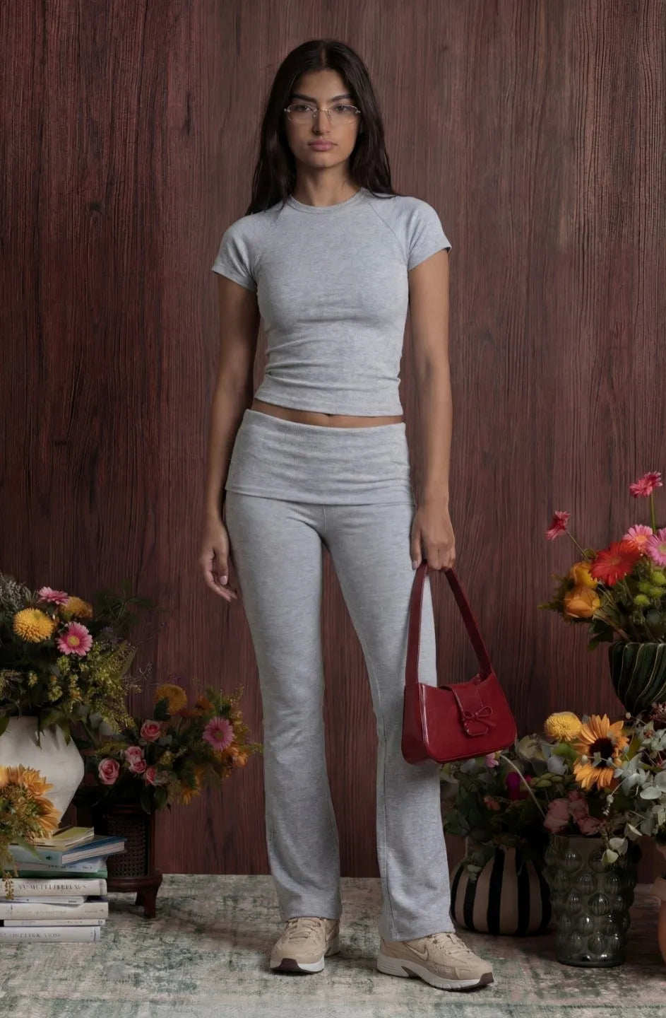 Woman in grey outfit holding a red bag with floral arrangements in the background