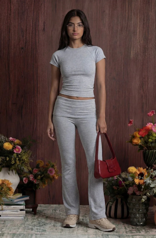 Woman in grey outfit holding a red bag with floral arrangements in the background