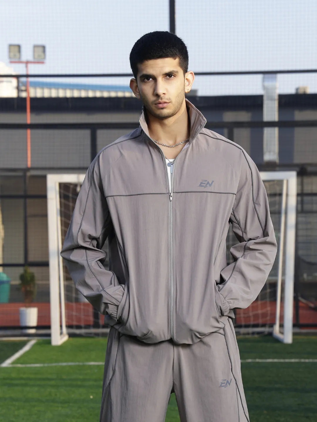 Person wearing a grey sports jacket  with a brand logo on a sports field.