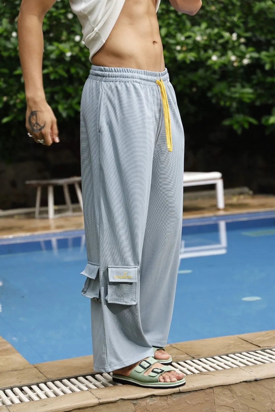 Person wearing light grey mesh pants with yellow accents by a poolside.