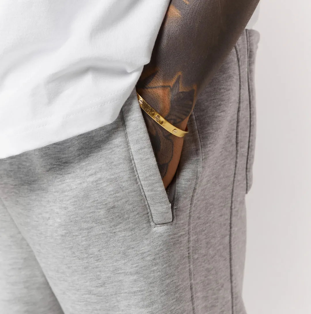 Grey jogger with a white shirt and tattooed arm on a light grey background