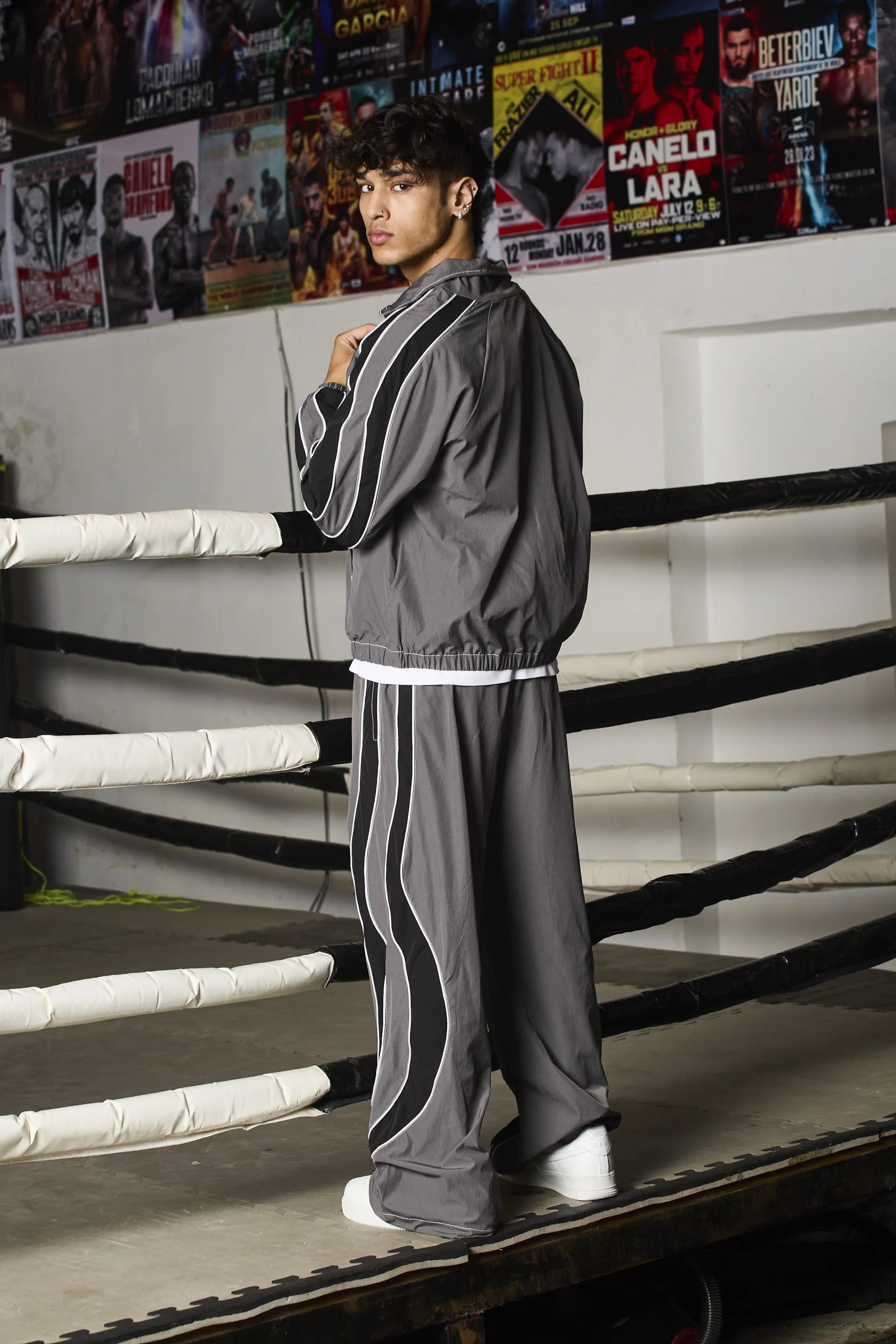Person in a tracksuit standing in a boxing ring with promotional posters in the background