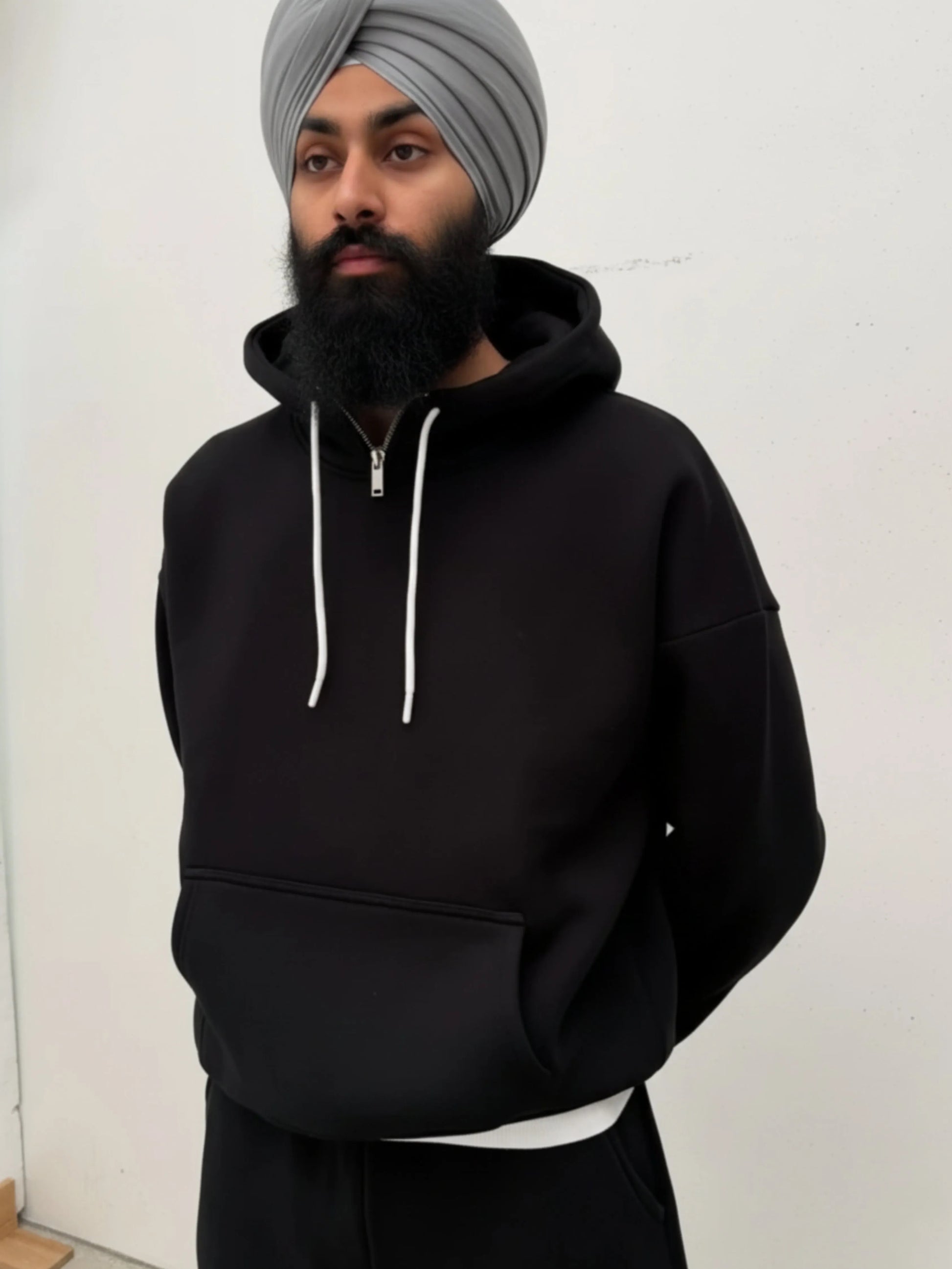 Person wearing a black hoodie and grey turban against a white background