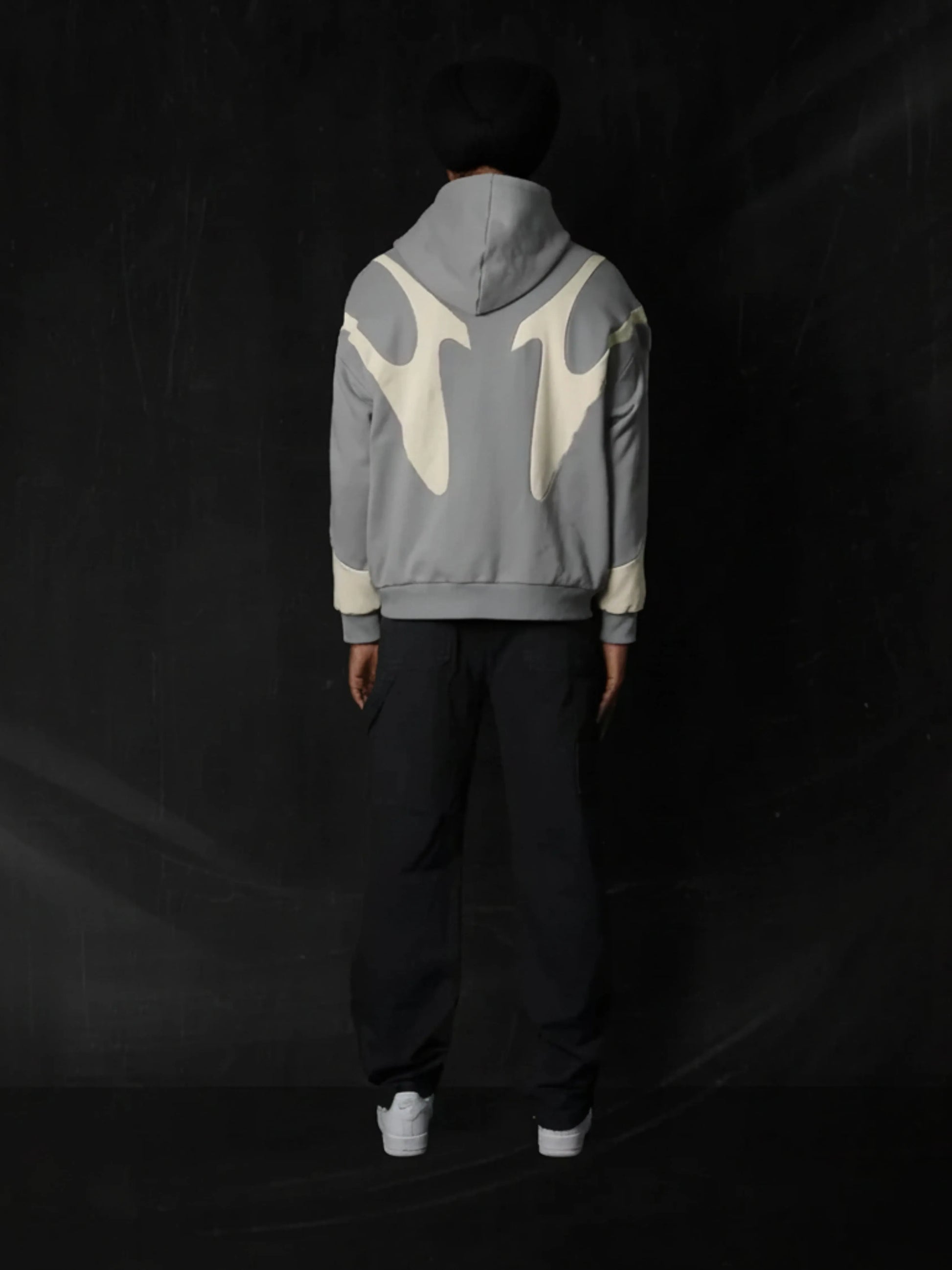 Person wearing a grey hoodie with white abstract designs on the back against a black background