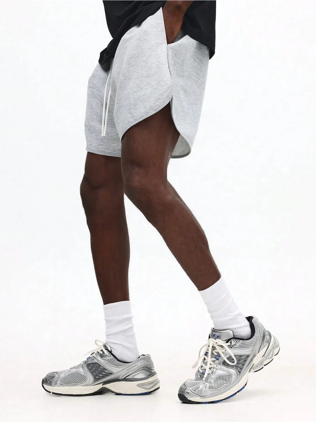 Person wearing grey athletic shorts, white socks, and grey sneakers on a white background