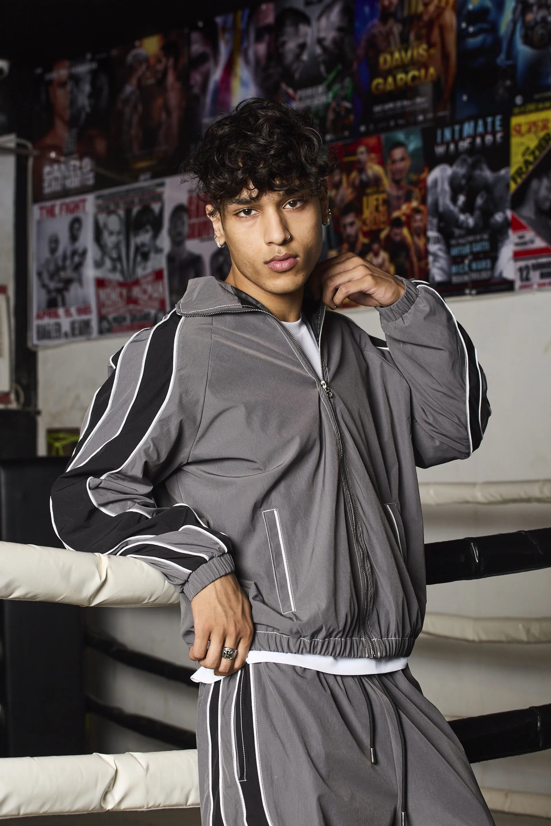 Person wearing a grey tracksuit in a boxing ring with posters in the background