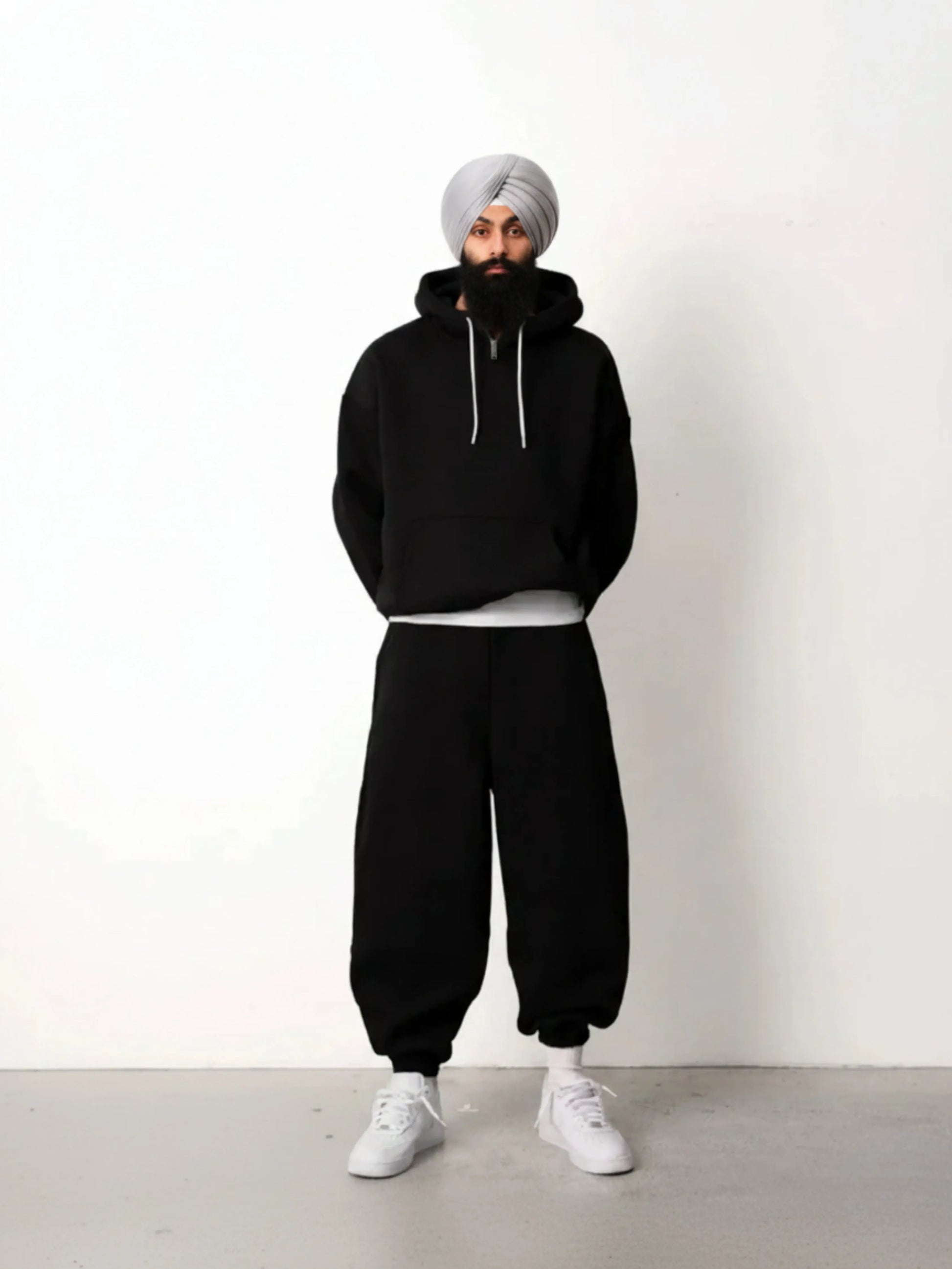 Person wearing a black hoodie and pants with a white turban against a white background