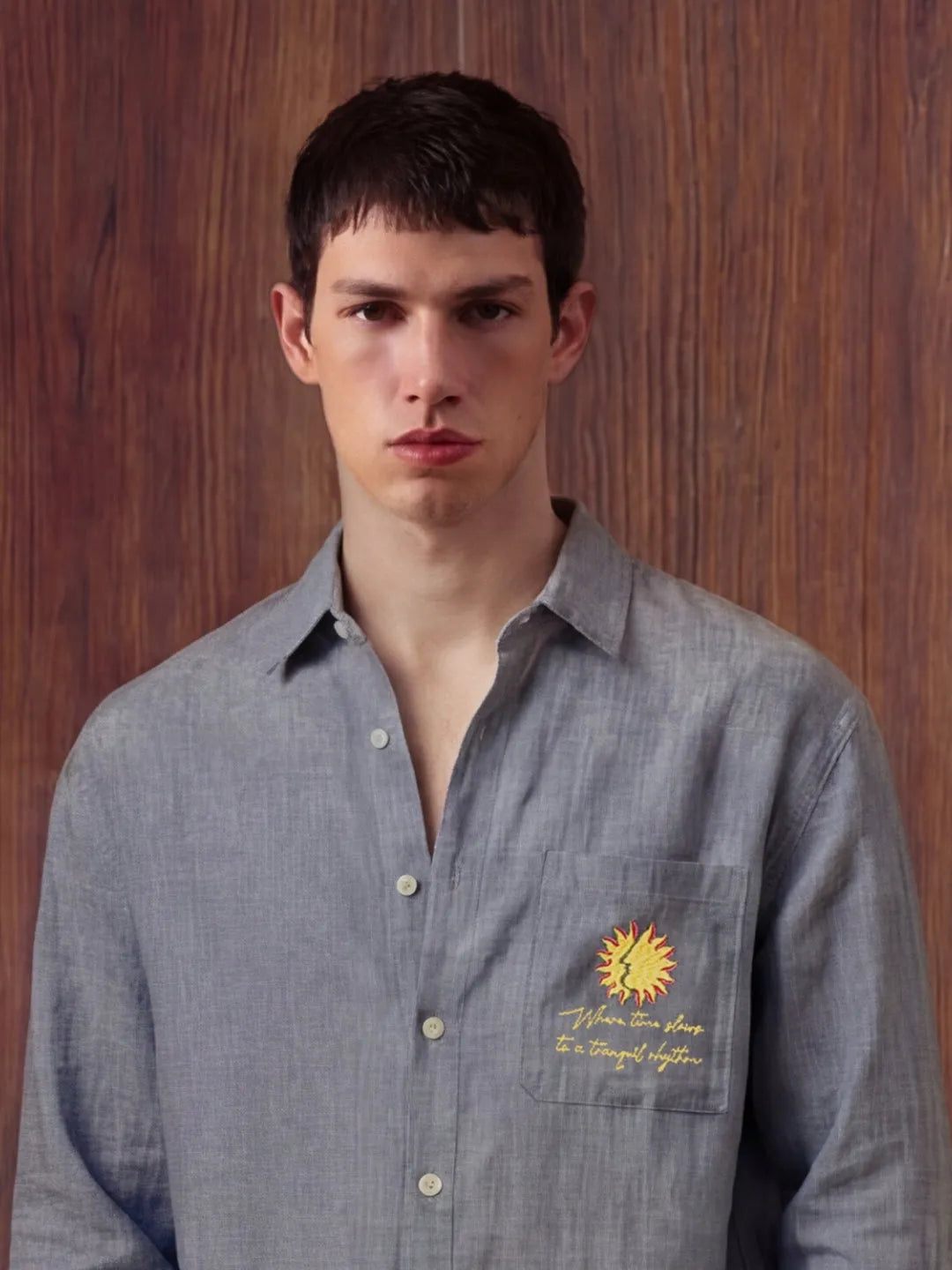 Man wearing a grey shirt with a sun design and text on a wooden background