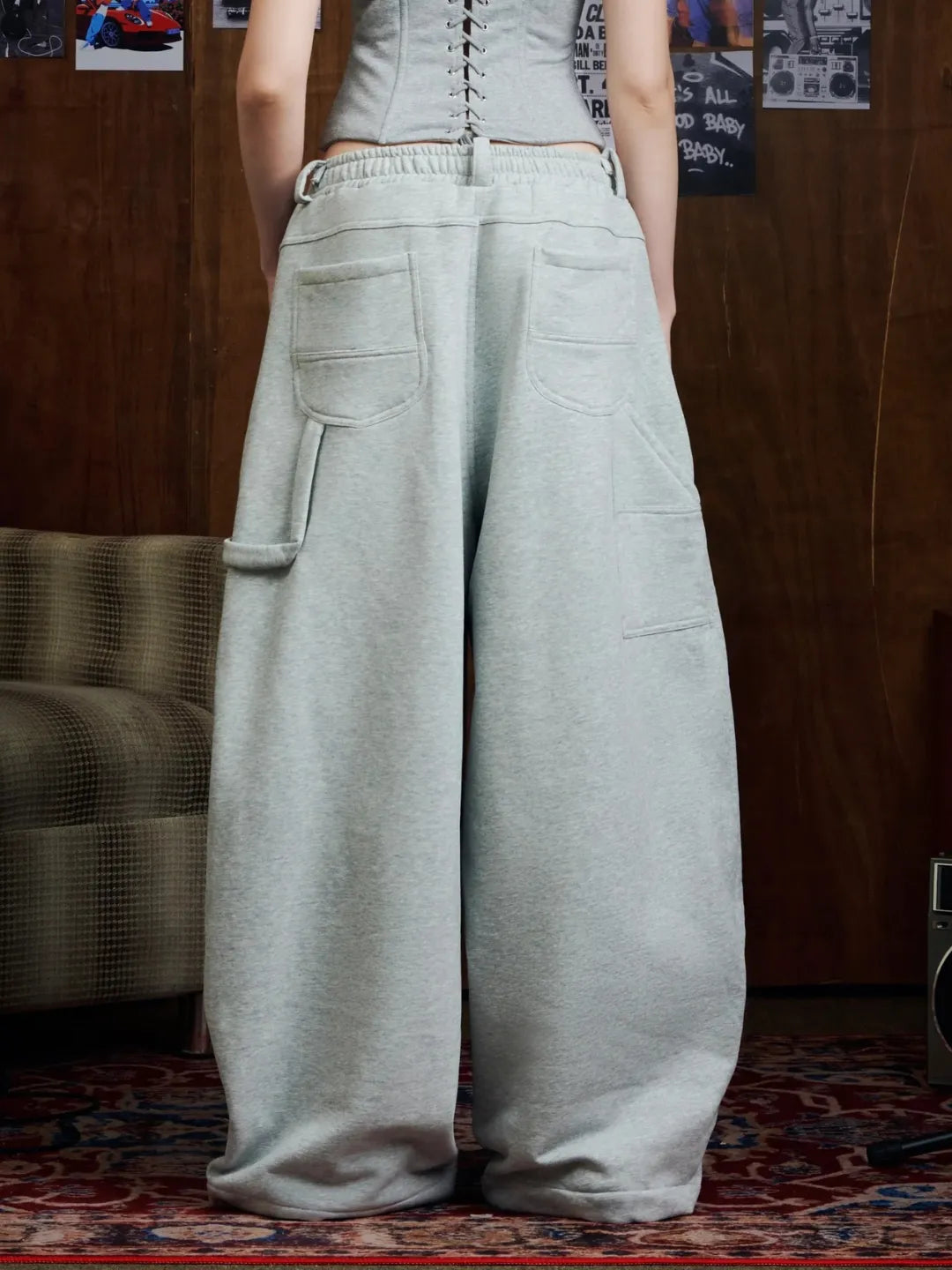 Person wearing light grey sweatpants in a room with a wooden wall and patterned rug.