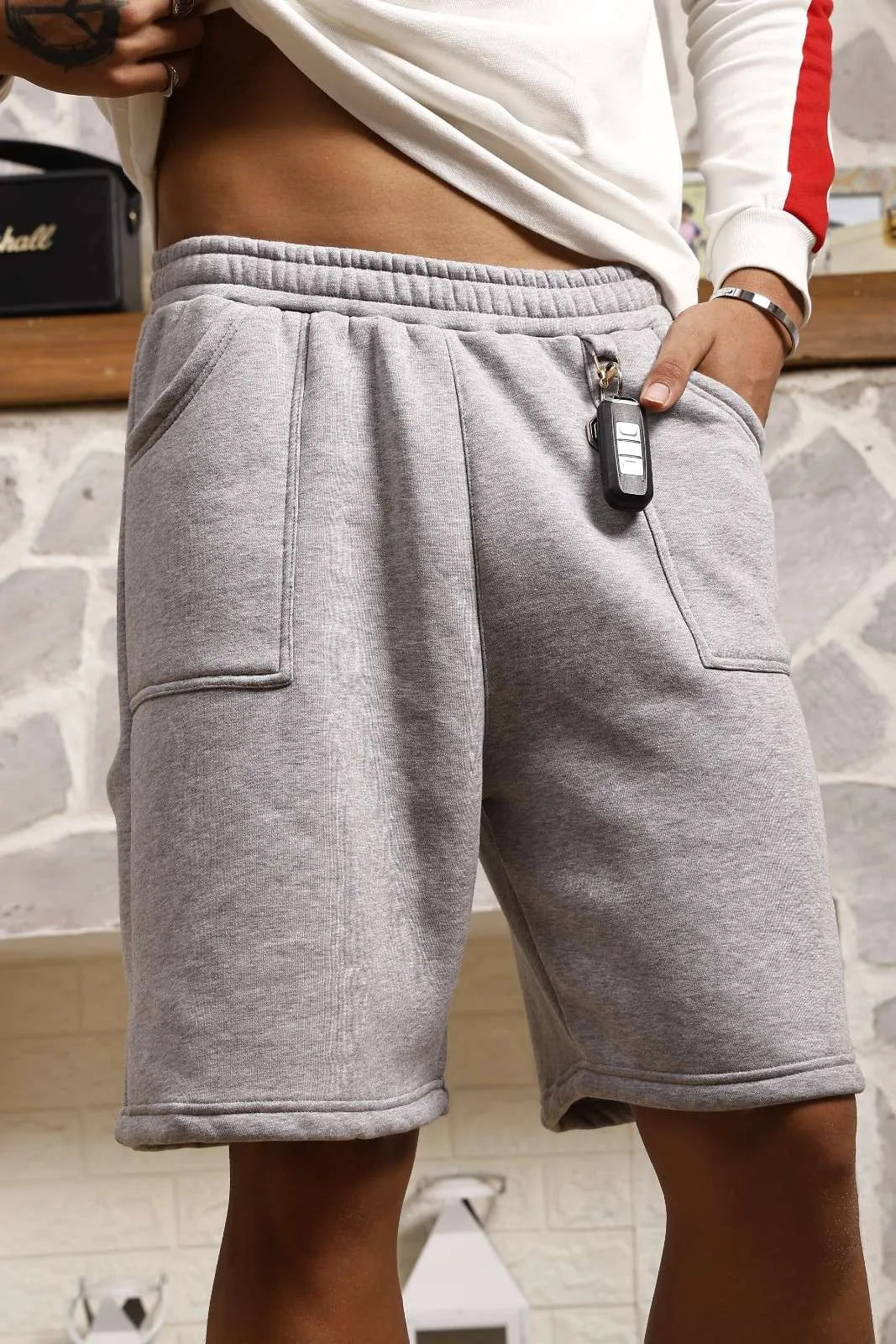 Person wearing grey sweat shorts with a stone wall background
