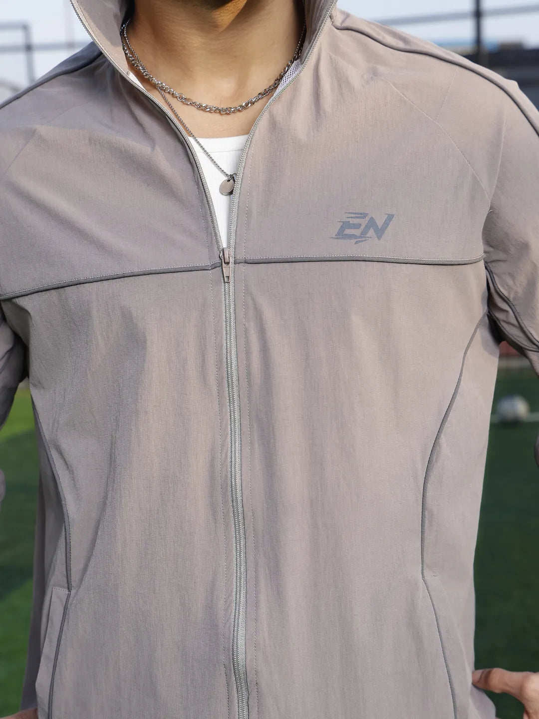 Person wearing a grey sports jacket  with a brand logo on a sports field