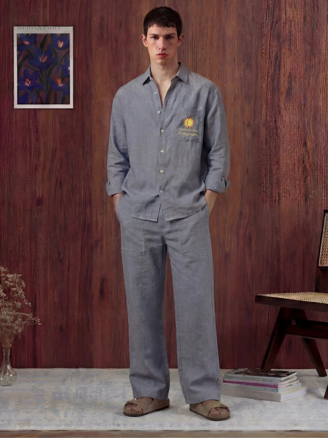 Man wearing a grey shirt and pants standing in a room with wooden walls and decor.