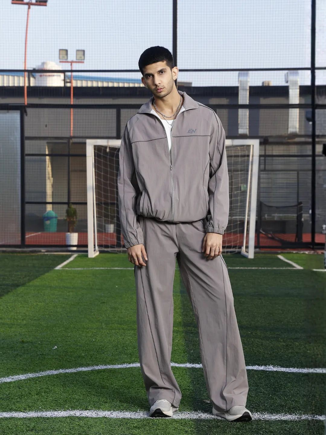 Man wearing a grey sports jacket standing on a sports field.