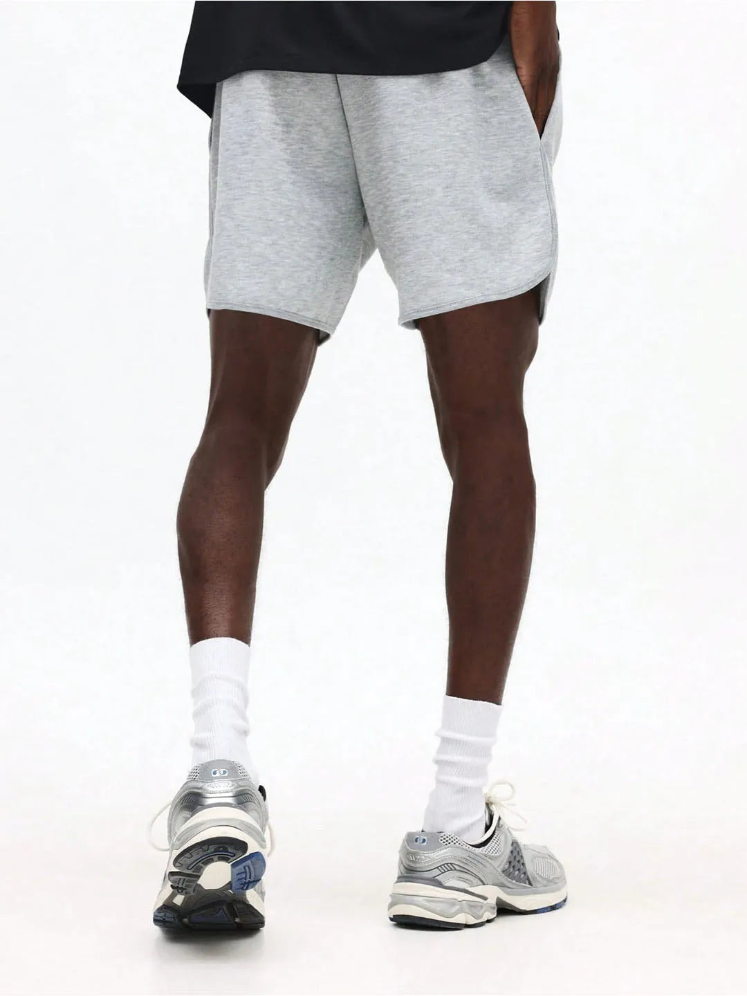 Person wearing grey shorts, white socks, and sneakers on a white background