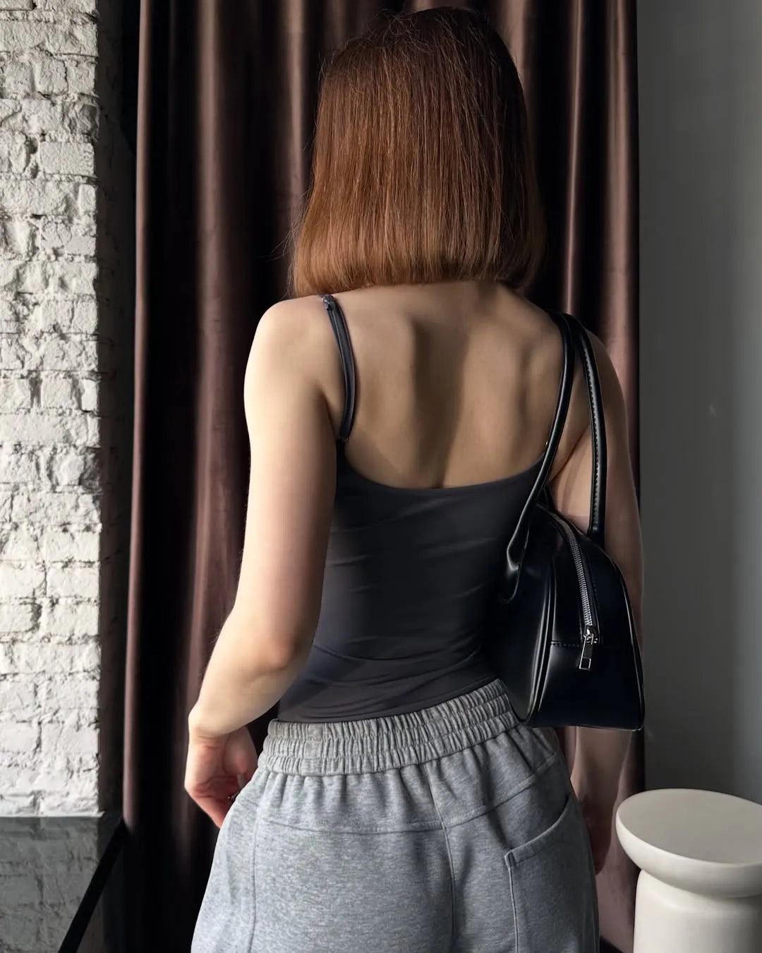 Woman in grey sweatpants standing against a brown curtain.