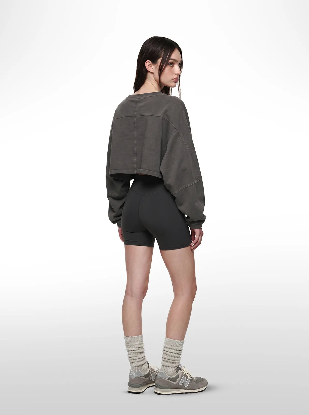 Person wearing a grey cropped t-shirt, black shorts, and gray socks on a white background