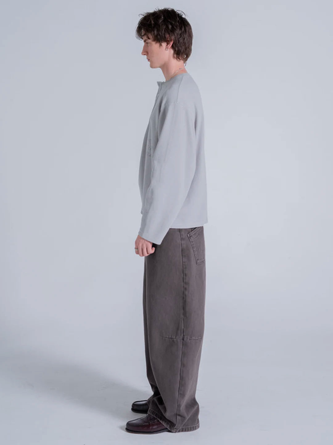 A model wearing a light grey long-sleeve crewneck t-shirt and dark grey wide-leg trousers