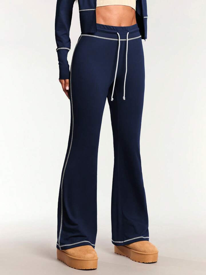 A woman standing and posing in a navy blue tracksuit, consisting of a zip-up jacket and leggings, with long sleeves and a pair of shoes visible.