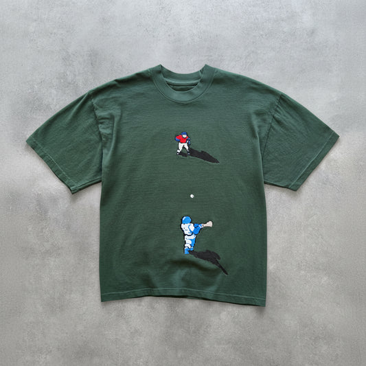 Green t-shirt with pixelated graphics of a baseball player on a grey surface