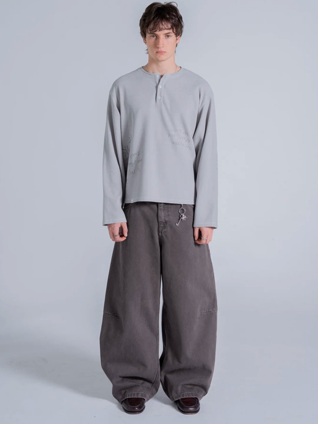 A model wearing a light grey long-sleeve henley-style t-shirt and very loose dark grey baggy pants.
