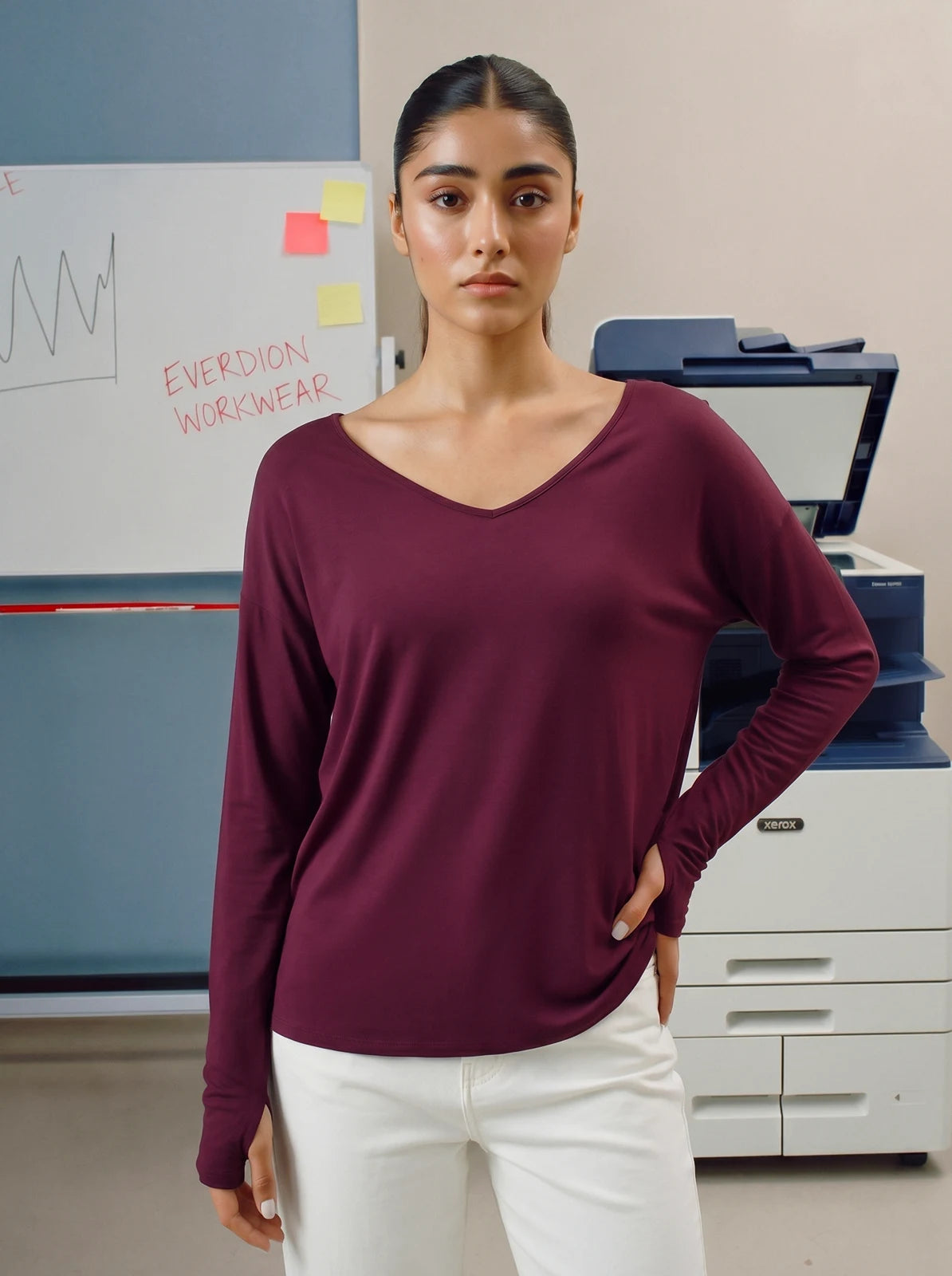Woman wearing a maroon long-sleeve shirt and white pants standing in an office setting.