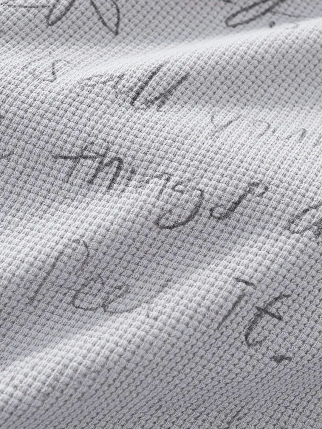 Close-up of a light grey waffle-knit fabric with a dark grey script pattern spelling out 'things are fine' across the surface.