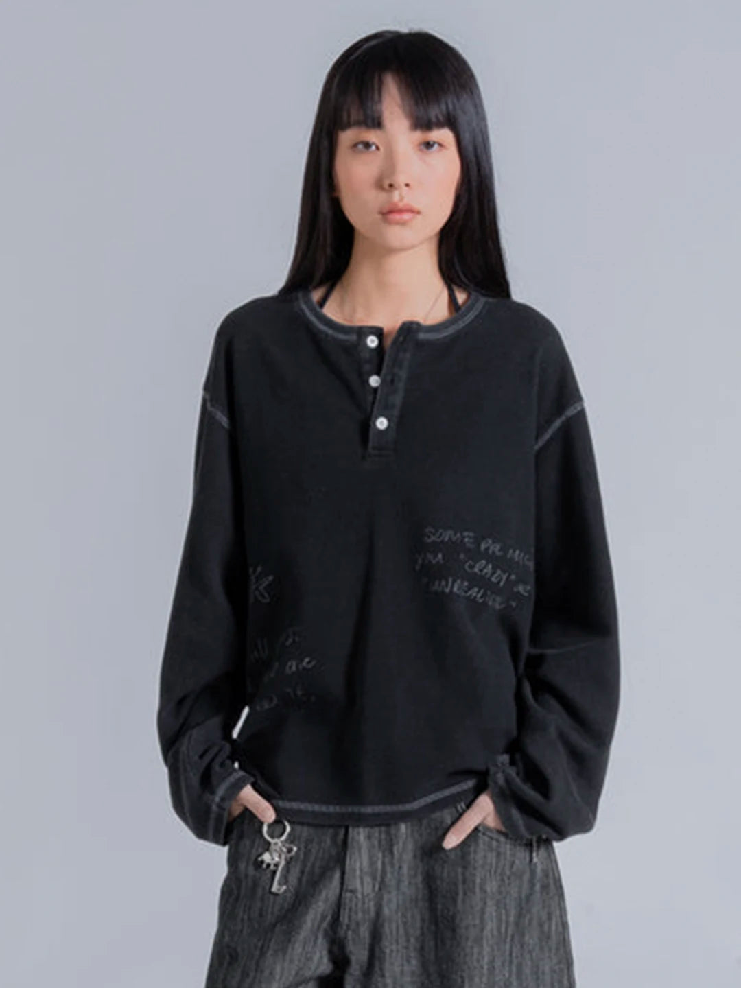 A model wearing a black long-sleeve henley tshirt with white script text on the front, paired with grey textured pants