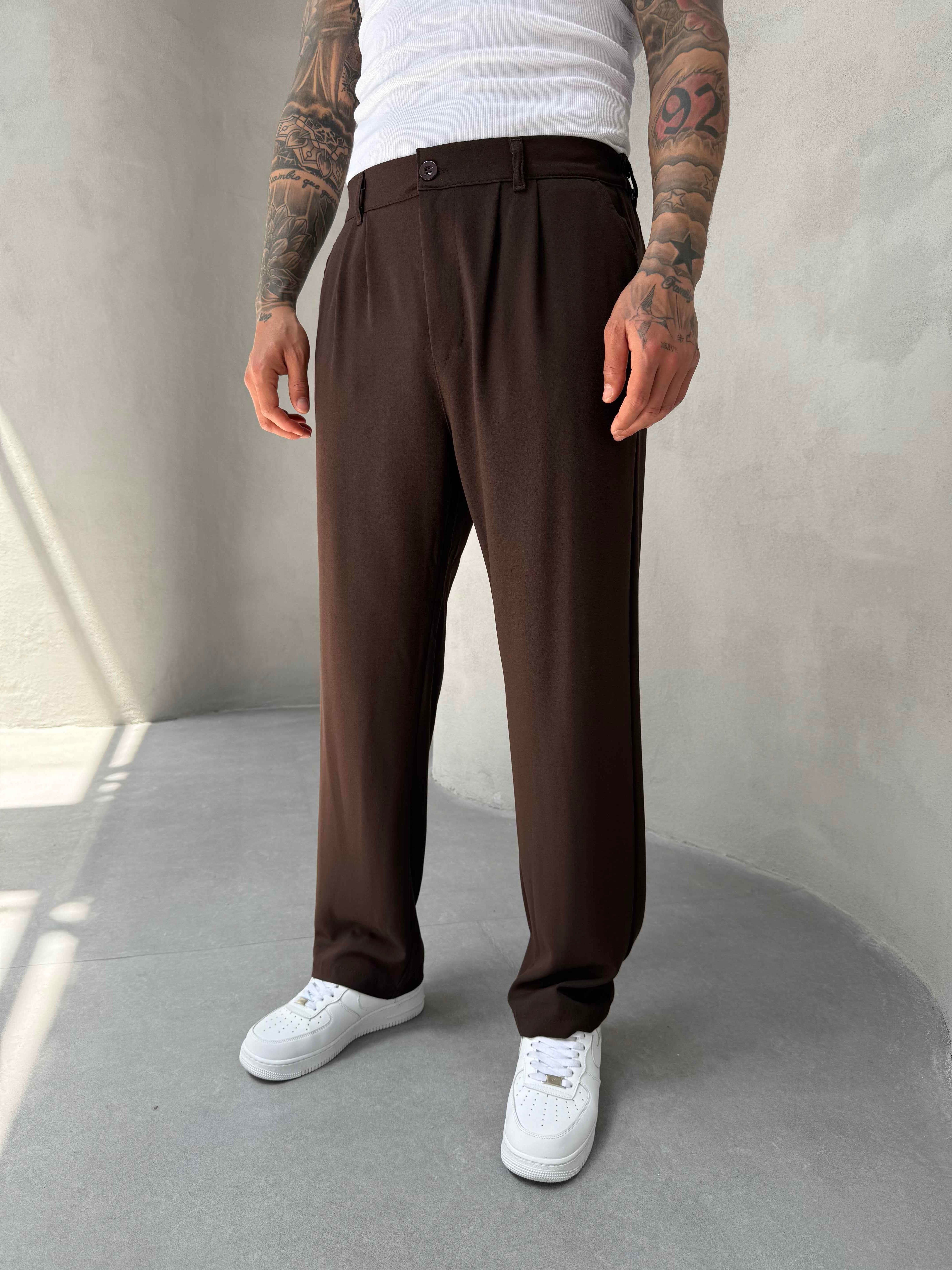 Person wearing brown pants and white sneakers against a plain background