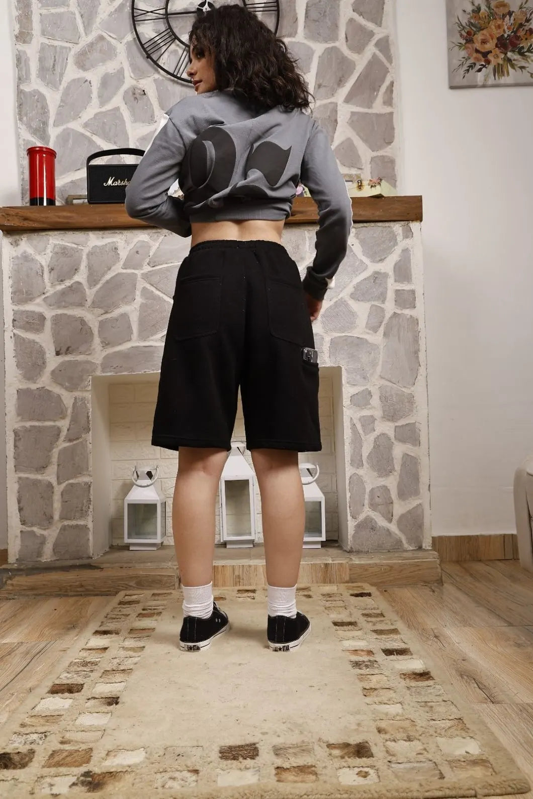 Person wearing a gray sweatshirt with a graphic design and black shorts in a room with stone walls.