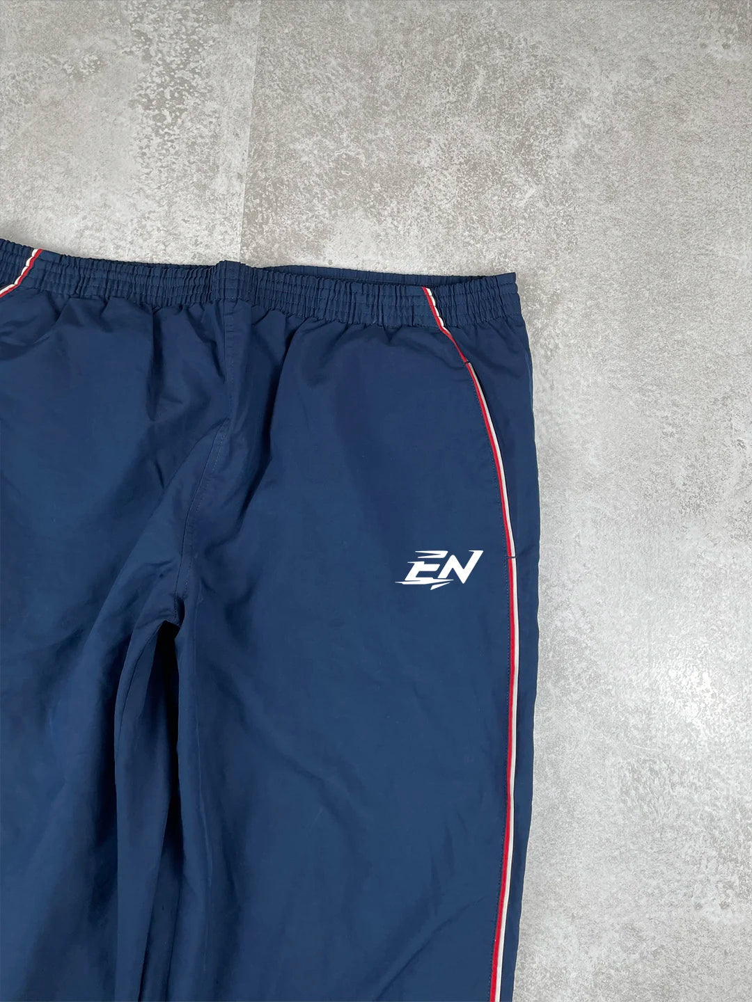 Navy blue athletic pants with a logo on a grey concrete floor