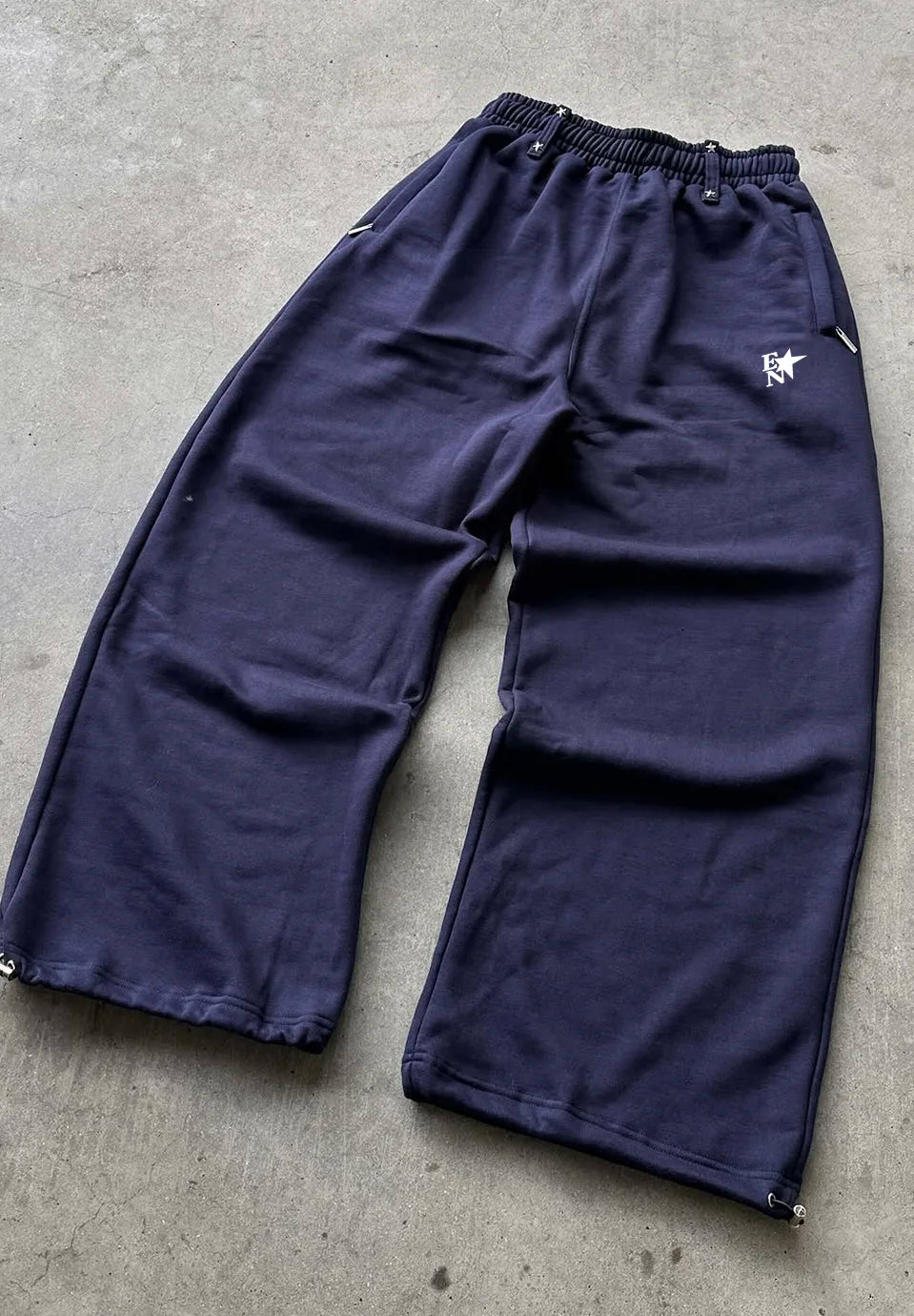 A pair of dark navy blue cropped sweatpants with an elastic waistband and a small white embroidered star logo on the left hip