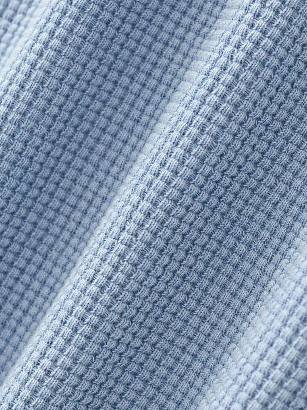 Close-up of a light blue waffle-knit fabric texture with soft diagonal folds.