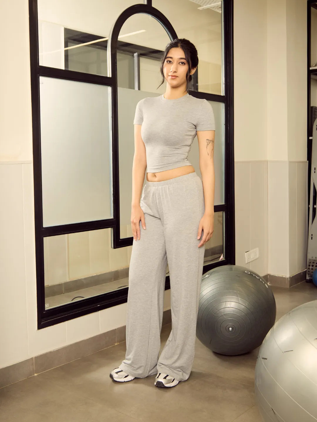 Woman in grey athletic wear standing in a gym setting with exercise balls.