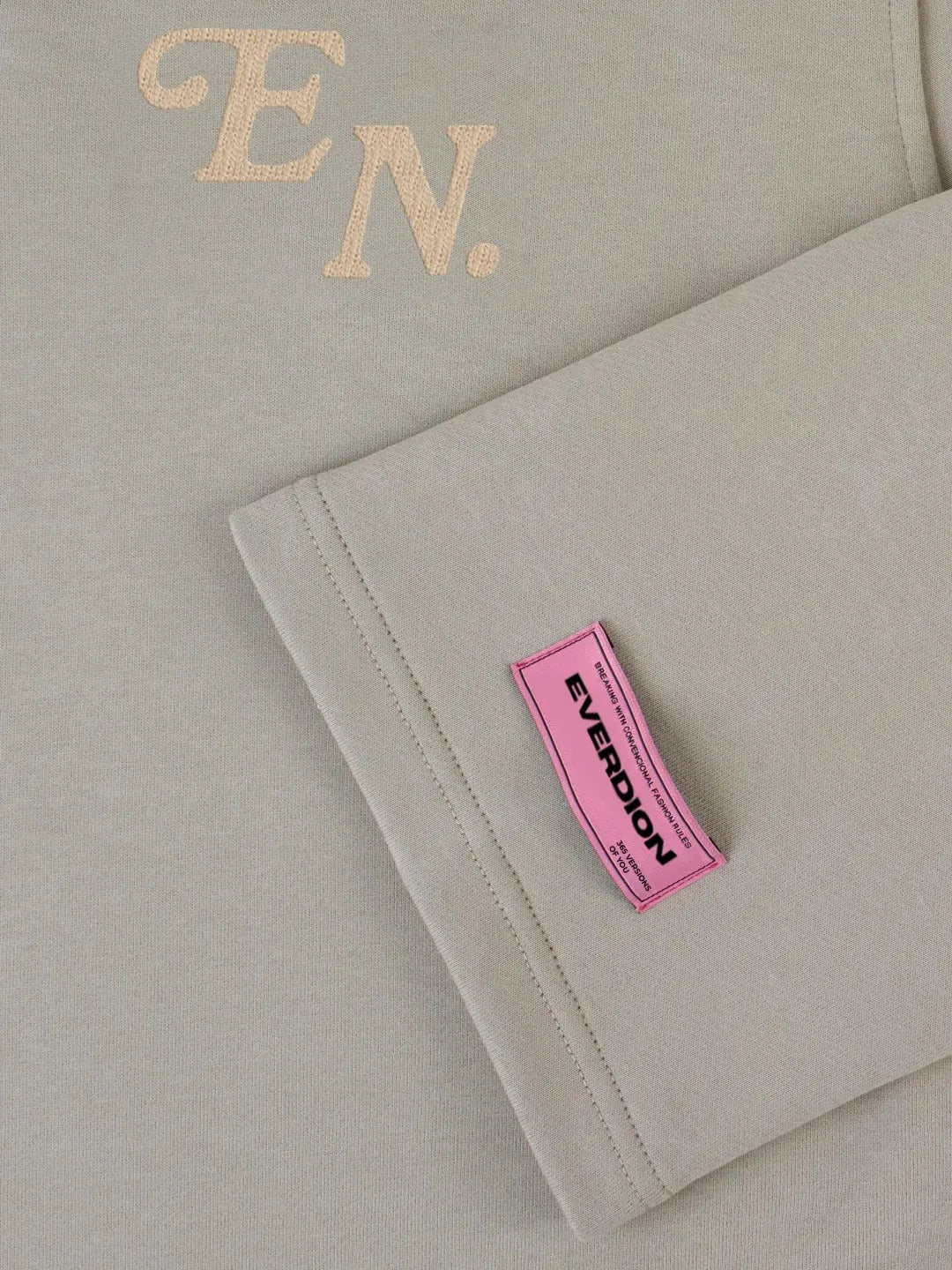 Grey fabric with 'EN' embroidery and a pink label on a beige background