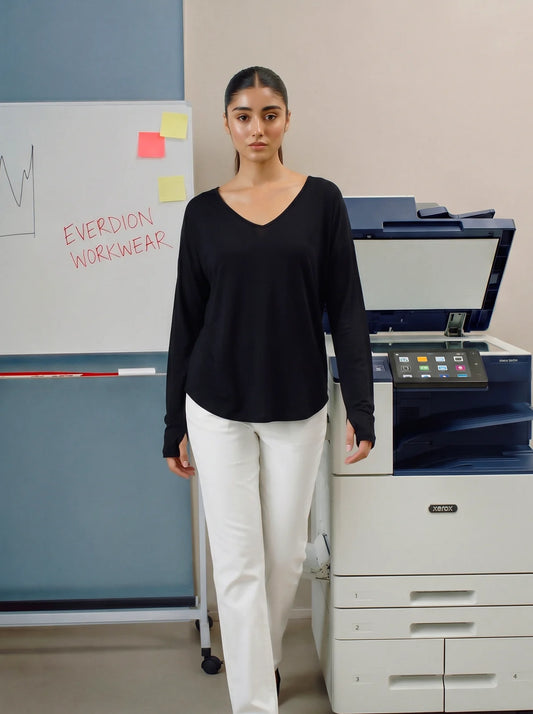 Woman in black top and white pants standing in front of a printer and whiteboard.