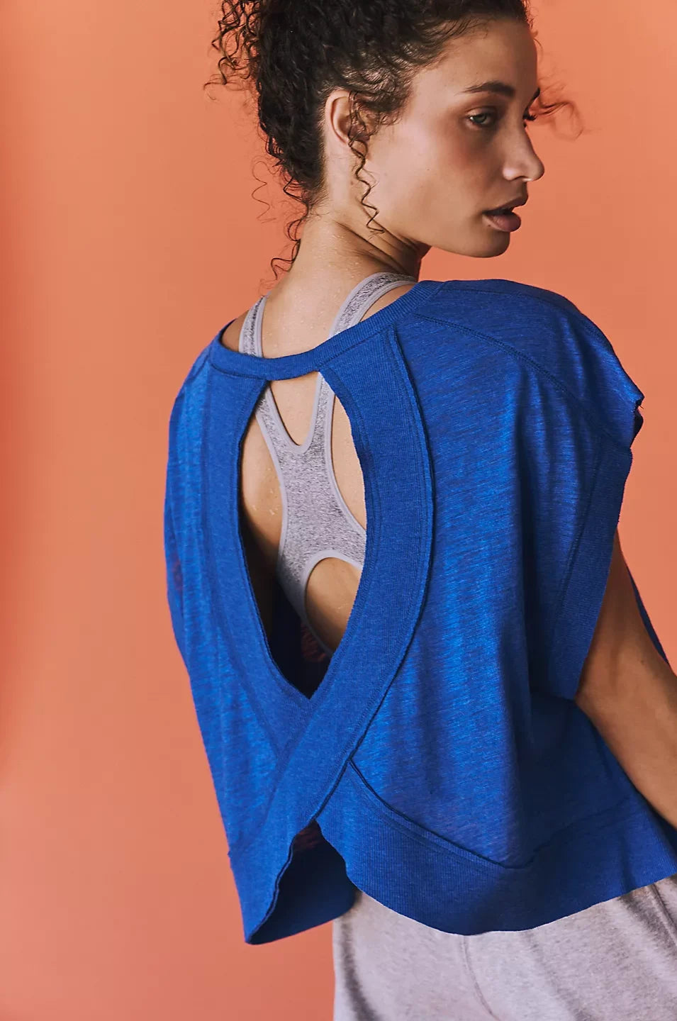 Woman wearing a blue open-back top against an orange background