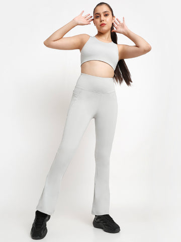 A female model wearing a grey sports bra and leggings, posing with one hand raised to her head.