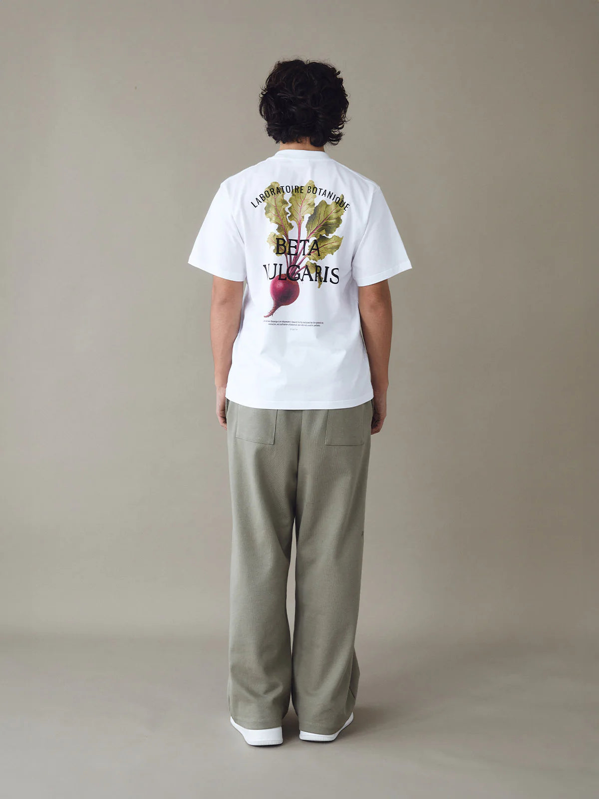 Person wearing a white t-shirt with a graphic design on the back against a beige background