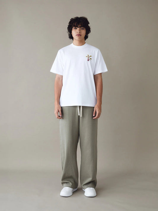 Person wearing a white t-shirt with a small graphic and beige pants on a plain background
