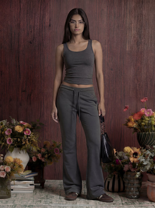 Woman in grey tank top and sweatpants standing in a room with floral arrangements.