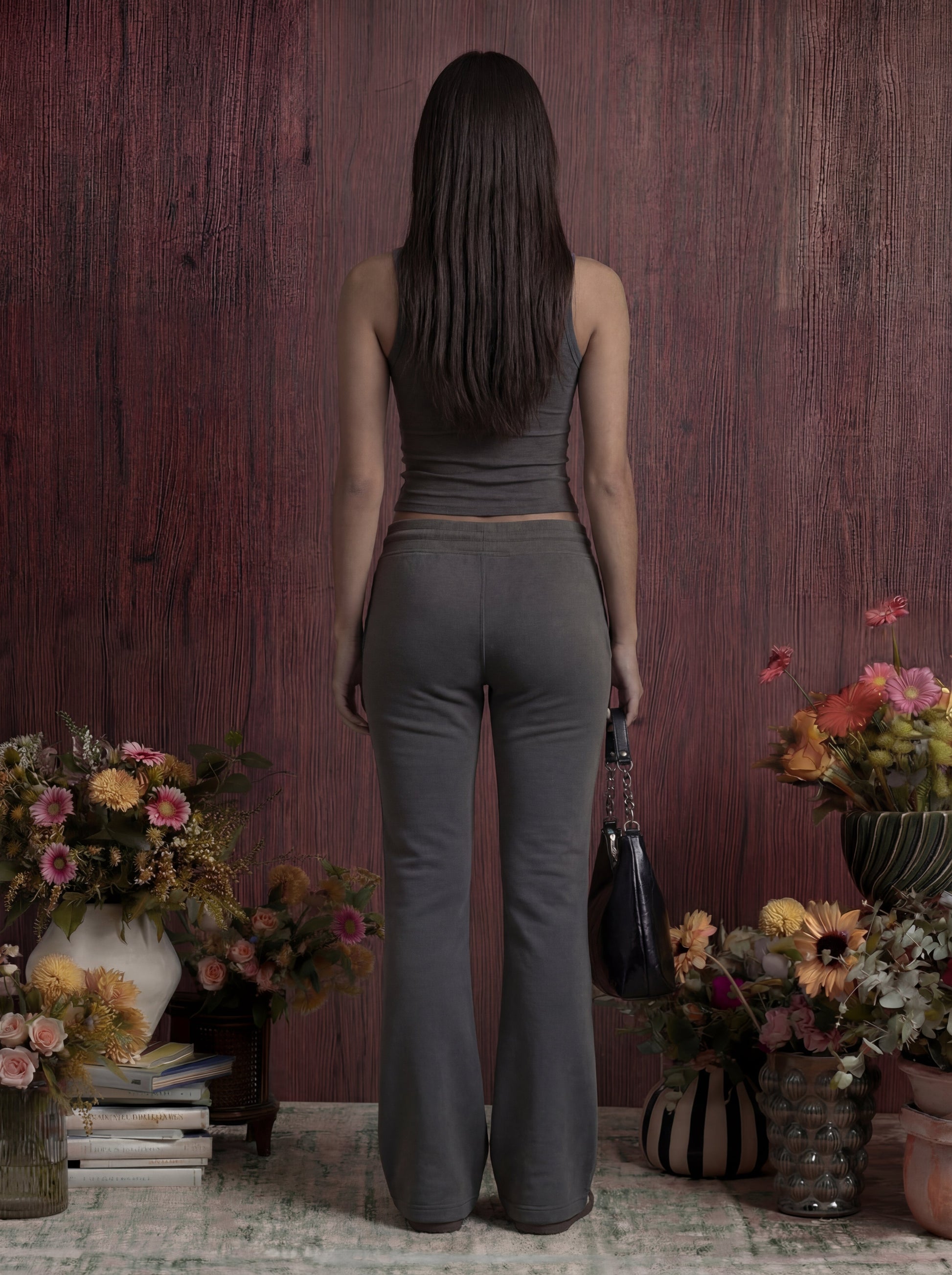 Woman in grey outfit standing in front of a wooden wall with floral arrangements.