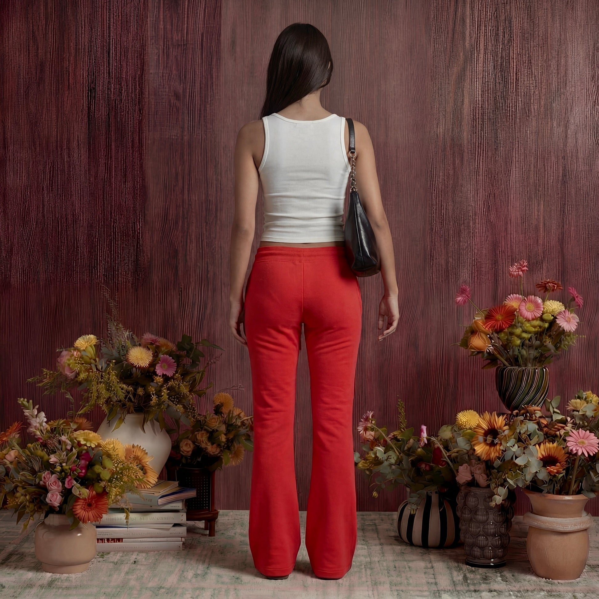 Woman in red sweatpants standing between floral arrangements against a wooden wall.