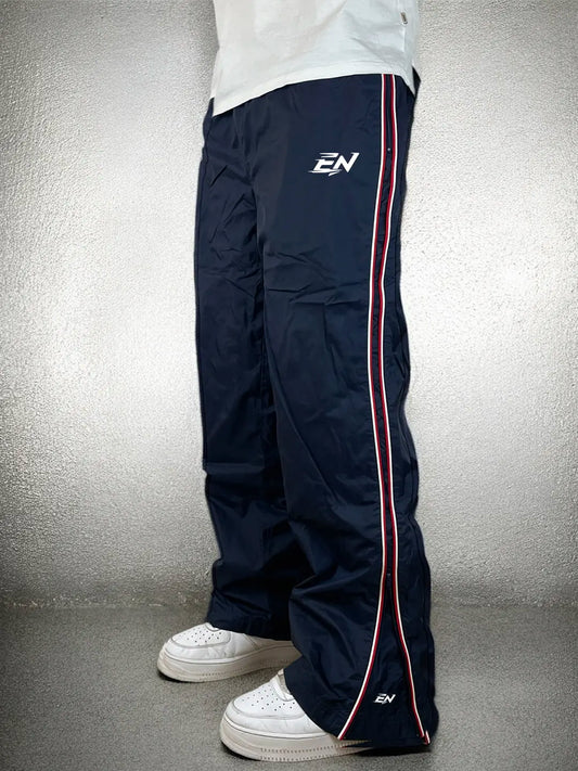 Navy track pants with a red stripe and brand logo on a grey background