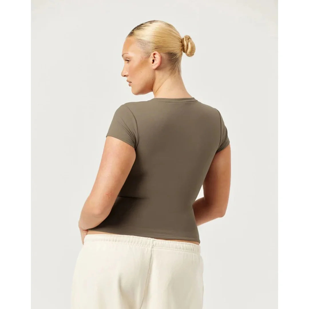 Woman wearing a green t-shirt and white pants on a light gray background