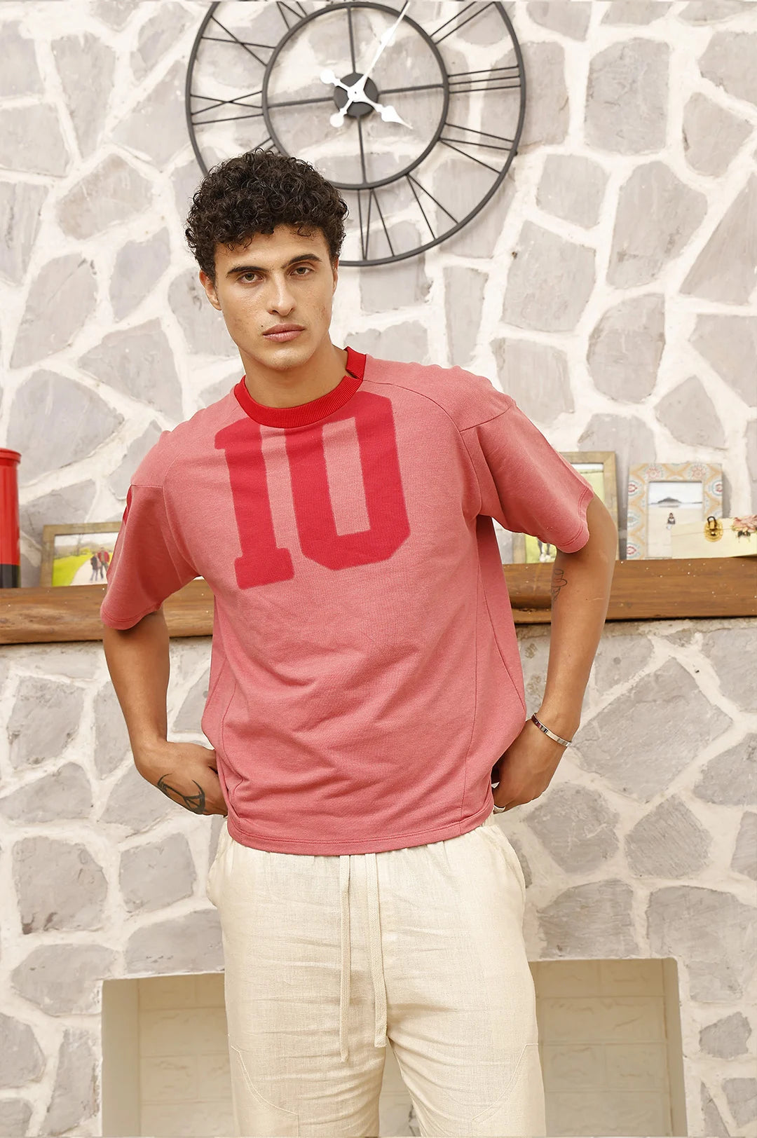 Man wearing a pink t-shirt with number 10 design against a stone wall.