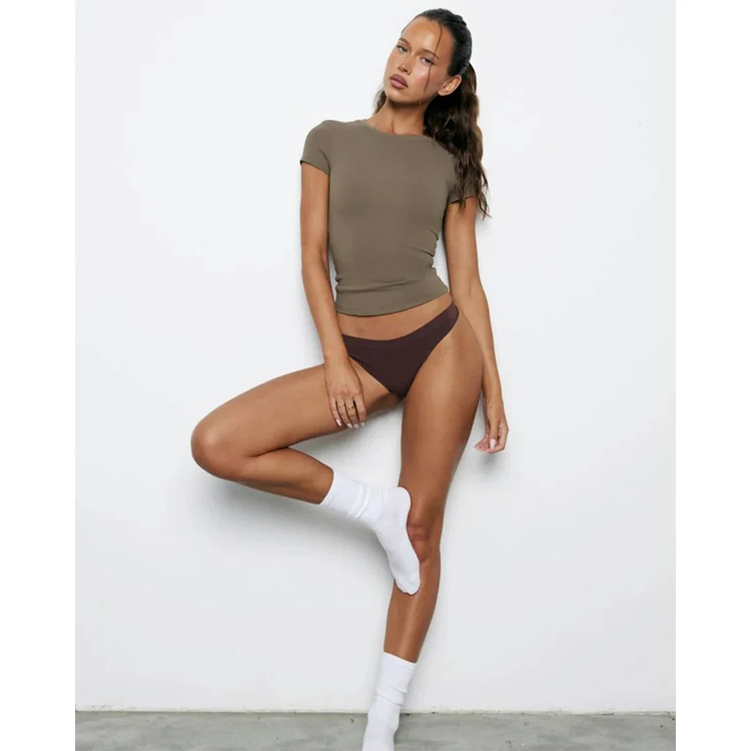 Woman wearing a brown top and dark brown underwear with white socks on a light gray background