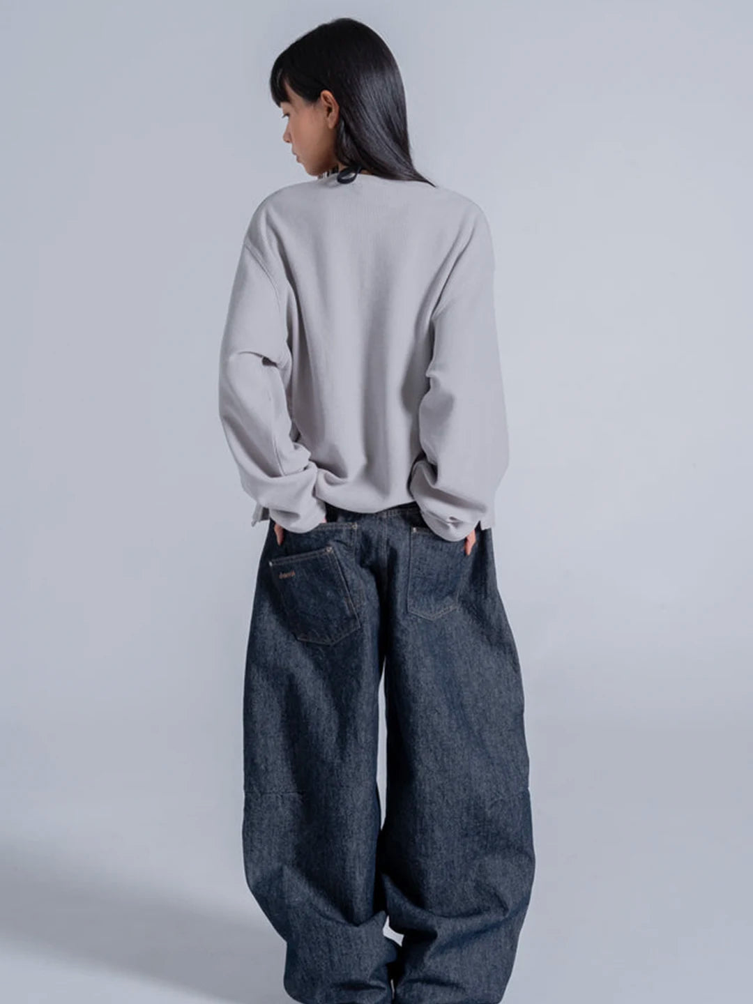 A model wearing a light grey oversized long-sleeve t-shirt and very wide-leg dark blue denim jeans 
