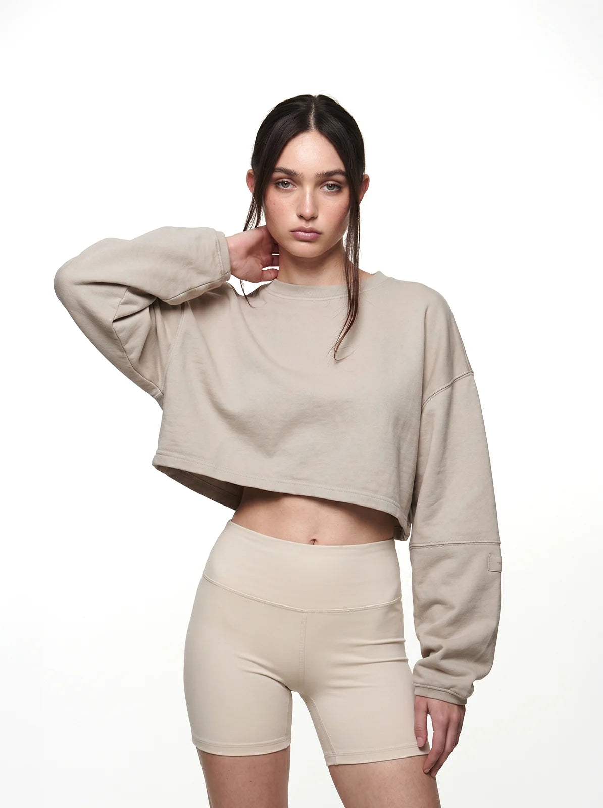 Woman wearing a beige cropped t-shirt and shorts on a white background
